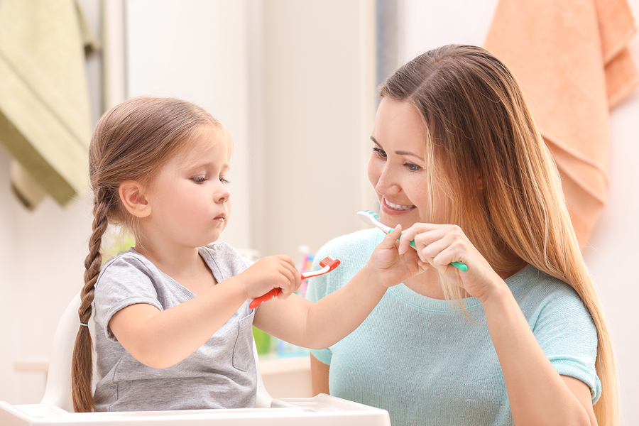 Mom Showing Toddler Daughter How to Use Toothbrush - The Super Dentists