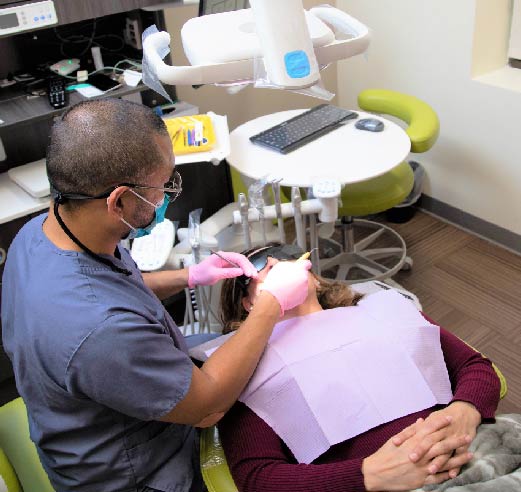 Adult Patient in Dental Chair getting Teeth Cleaned by Dentist - The Super Dentists