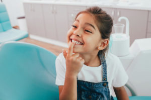 Young Child Pointing to Her Teeth while Sitting in Dentist Chair - The Super Dentists