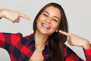 Teen Girl with Brown Hair in Plaid Shirt Smiling and Pointing to Braces - The Super Dentists