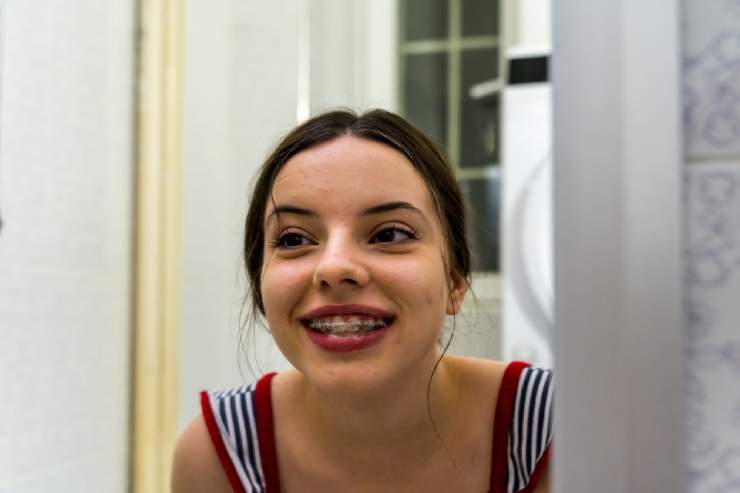 Teen Girl Wearing Braces Looking in Mirror and Smiling - The Super Dentists