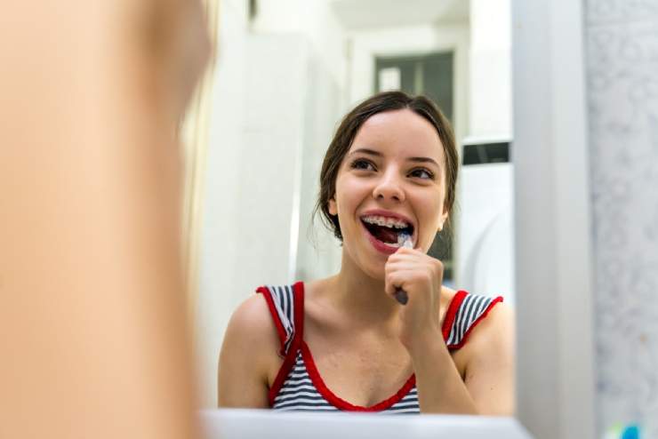 Teen Girl Looking in Mirror while Brushing Teeth with Braces - The Super Dentists