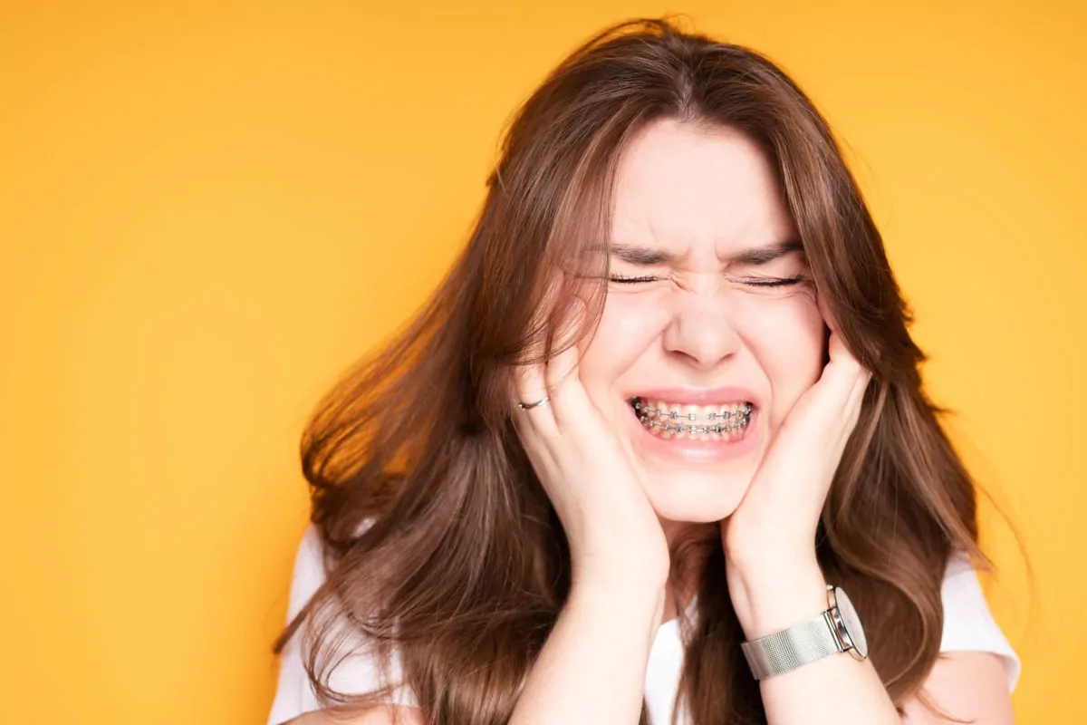 Young Girl Wearing Braces Holding Cheeks from Braces Pain - TSD