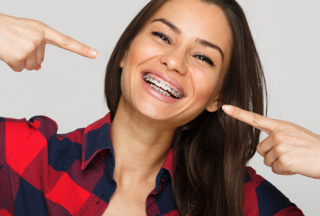 Teen Girl with Brown Hair in Plaid Shirt Smiling and Pointing to Braces - The Super Dentists