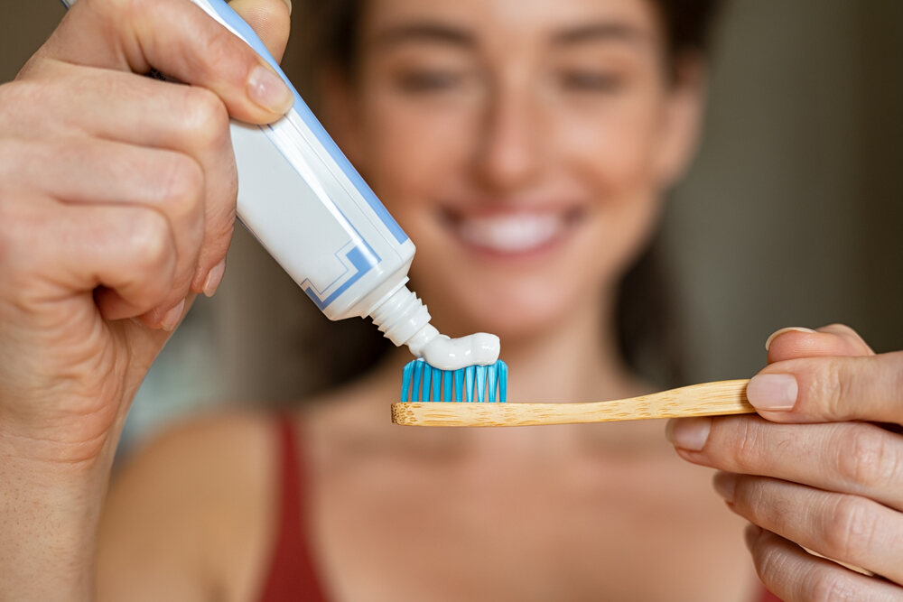 Woman puts toothpaste with hydroxyapatite onto natural bamboo toothbrush 
