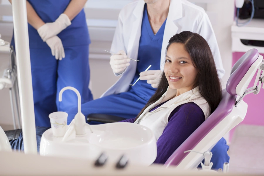 A young Latino woman at the dentist for teenagers, smiling from the dental chair and looking into the camera.