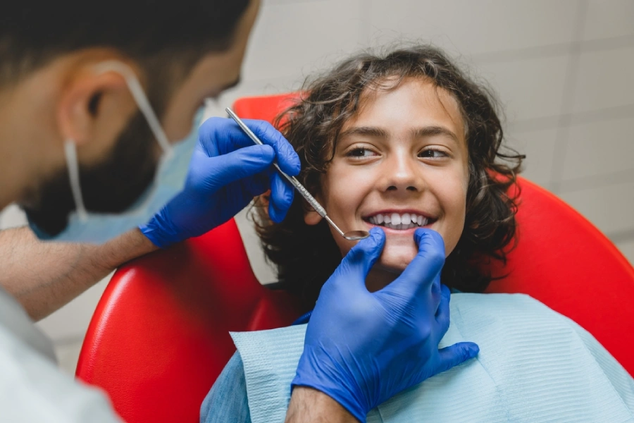 A young adolescent smiles as their dentist for teens begin to examine their teeth.