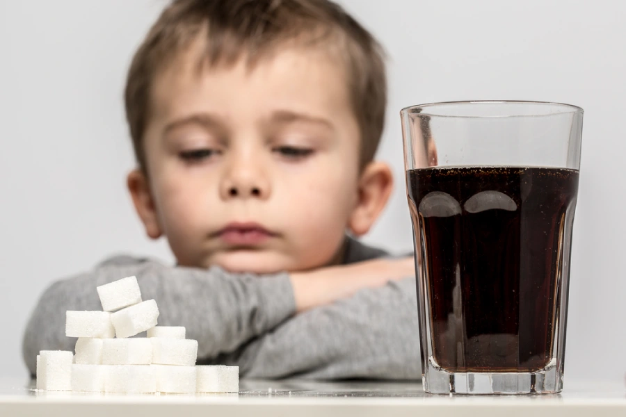 Kid looking at a soda with sugar next to it