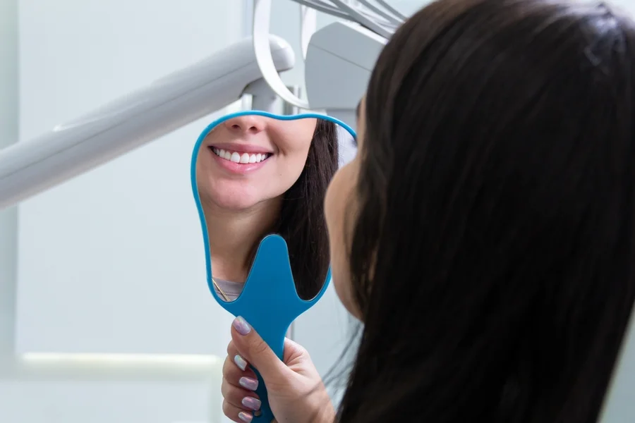 caucasian female smiles in mirror at dentists’ office after a favorable experience