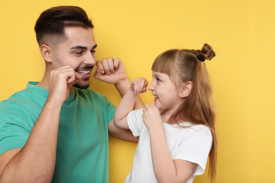 Father and daughter floss their teeth together to help prevent receding gums