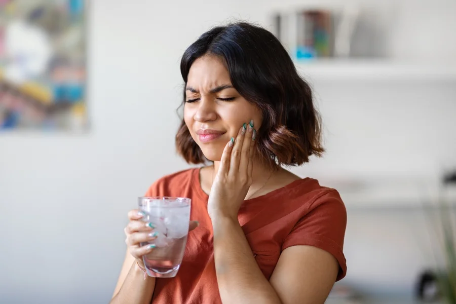 Young woman experiences sensitive teeth due to a combination of teeth whitening and drinking cold ice water