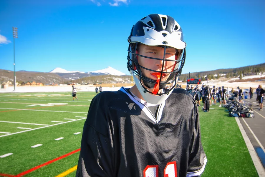 A young male teenage lacrosse player wears a mouth guard
