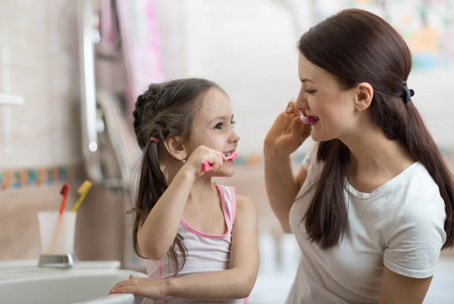 Mom brushing teeth with young daughter