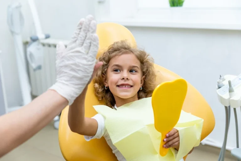 Young girl holding bright yellow mirror in yellow chair high high-fives dentist while smiling