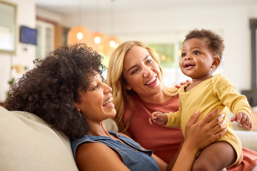 Same-sex female couple smiles holding baby after a pleasant experience at a local family dentist’s office in San Diego