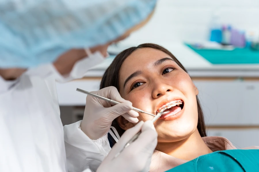 Orthodontist examines teen female patient’s braces