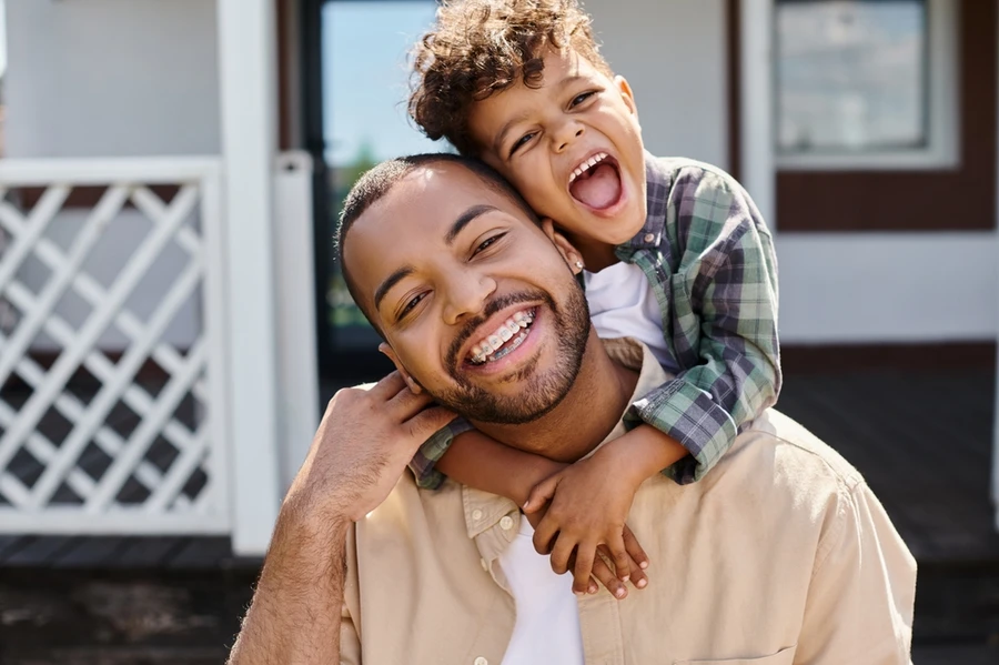 Young father carrying his son on his back smiles while wearing braces