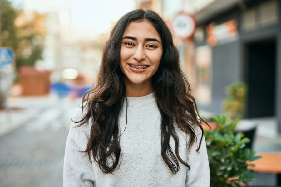 Teenage girl in gray sweater smiles while wearing braces