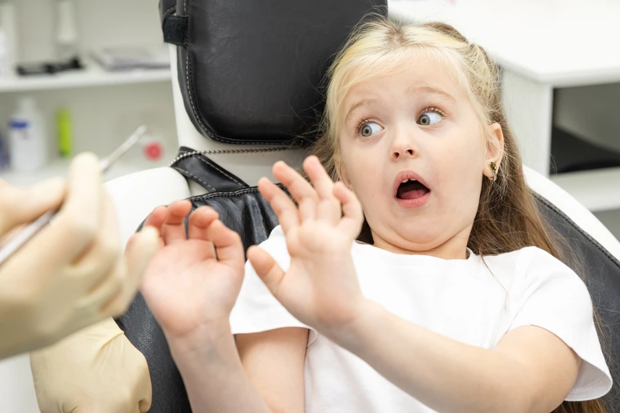 Little girl afraid of the dentist puts hands up