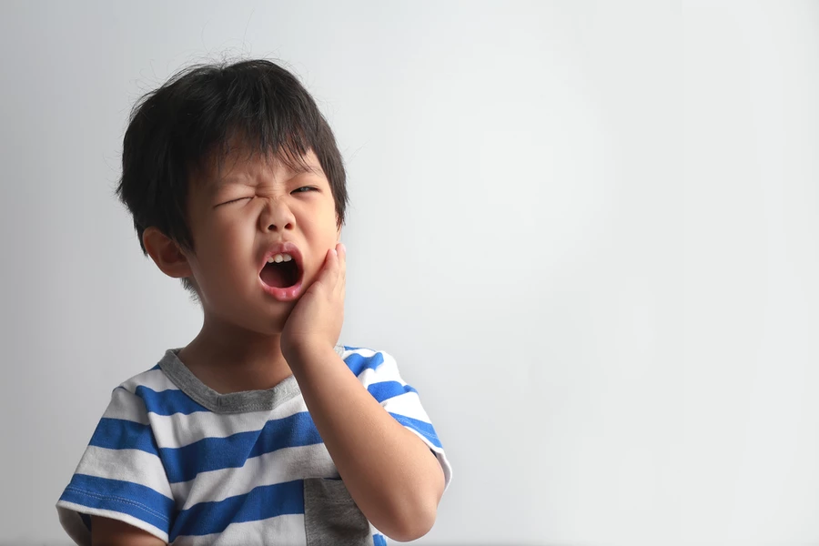 Little boy in blue and white striped shirt grabs his face in pain due to a toothache