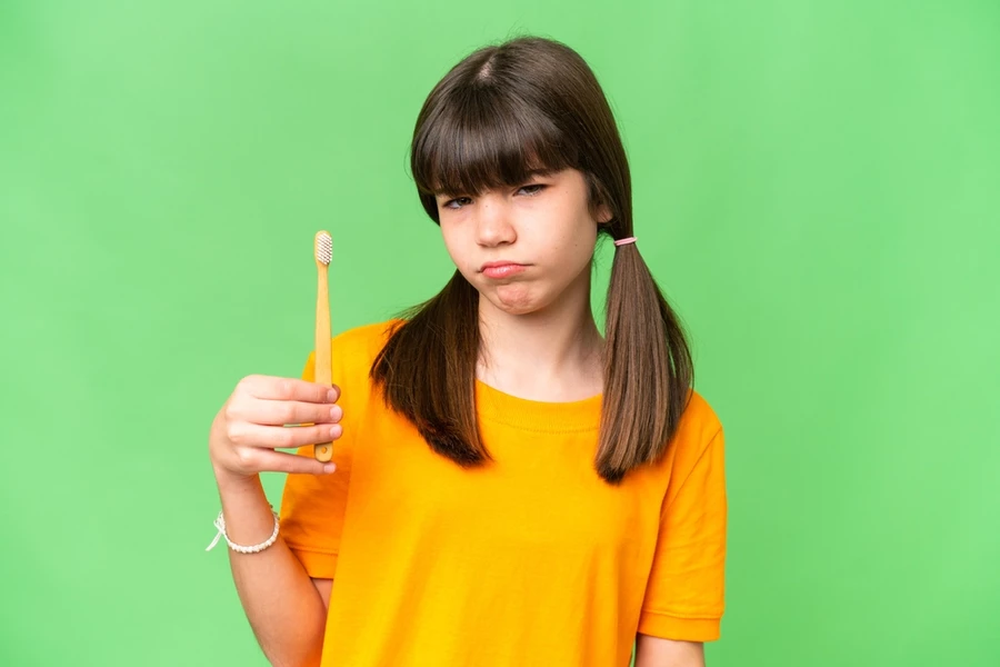 Young girl pouts holding up a toothbrush