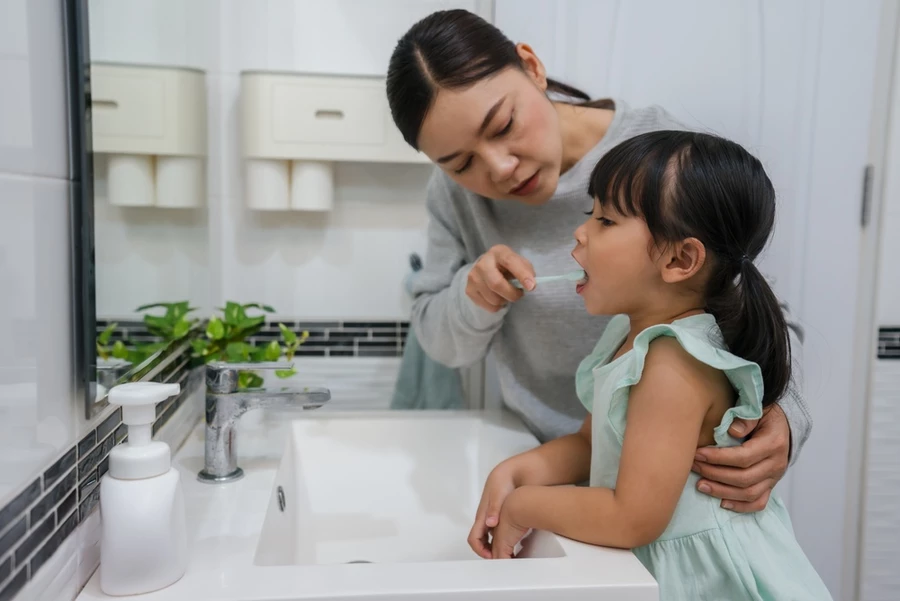 Mother helps young child brush her teeth