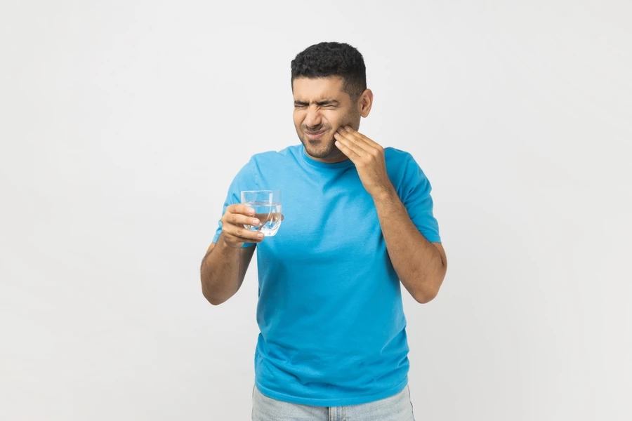 Man grimaces due to sensitive teeth that have been activated by drinking cold water