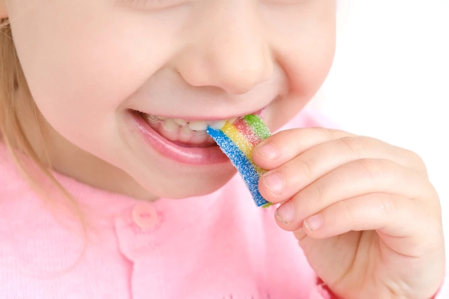 Close up of a young girl eating a rainbow colored sugary snack