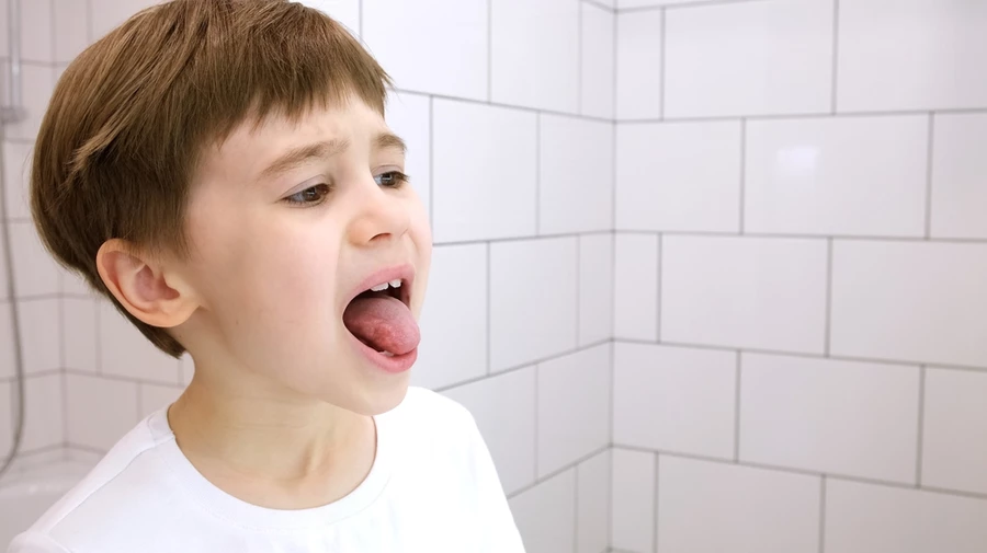 Young boy sticks his tongue out between his teeth and slightly frowns