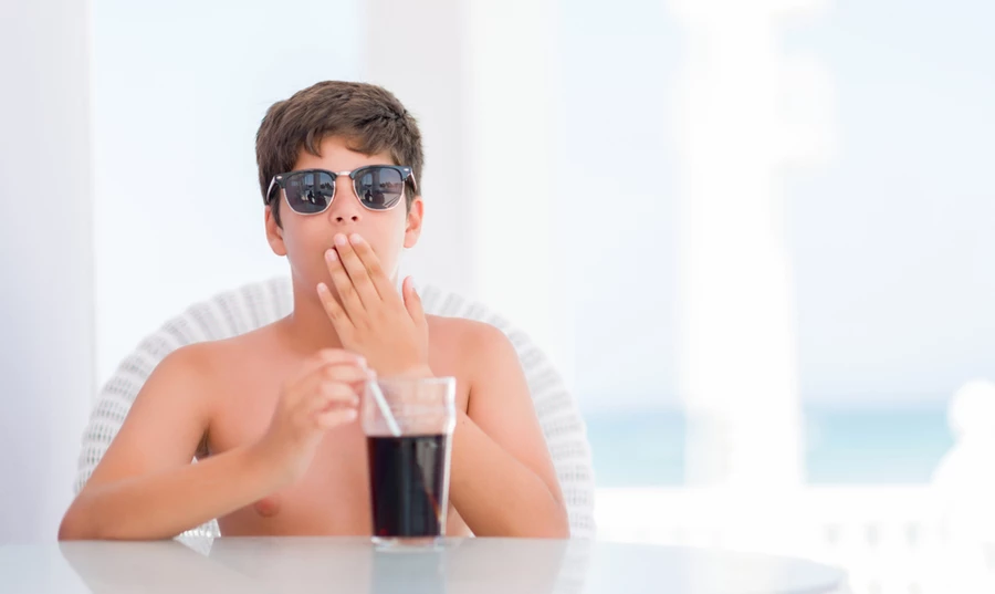 Young teenage boy with sunglasses covers his hand while belching after drinking a glass of sugary soda